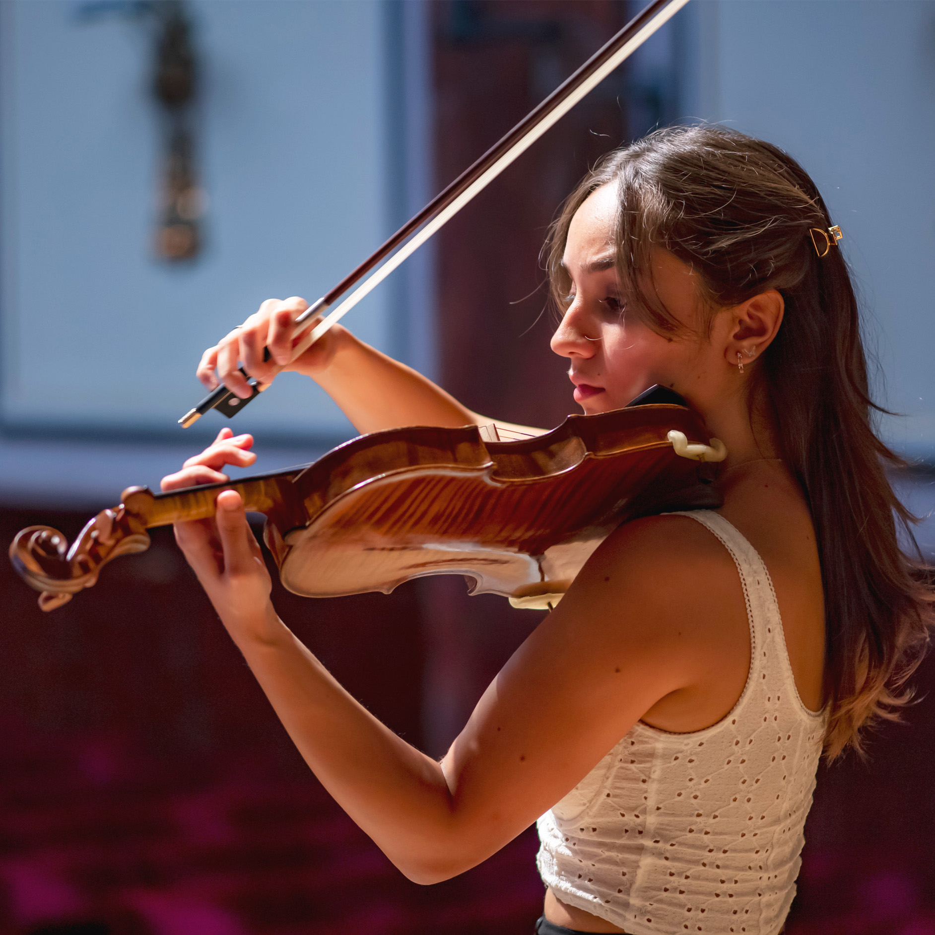 Female student, wearing a white summer shirt, playing the violin in a solo performance.